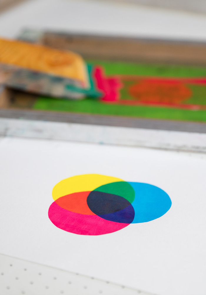 Three overlapping circles in yellow, magenta, and cyan are printed on white paper, with a screen printing tool in the background—an ideal snapshot from our Beginners' Screen Print Workshop (£75pp).