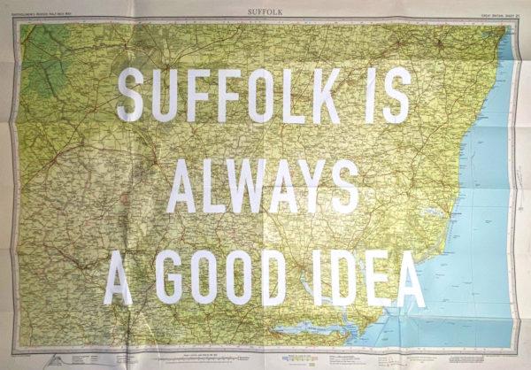 A beautifully crafted map of the Suffolk region transforms into a striking work of art with the phrase "SUFFOLK IS ALWAYS A GOOD IDEA" prominently emblazoned in large white letters. This artistic piece intricately highlights the geographical features of Suffolk, blending cartography with elegant design to create a captivating visual representation.