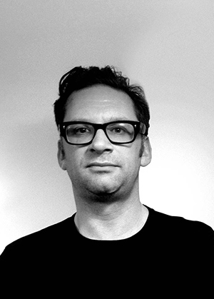 Black and white portrait of a person with short dark hair, glasses, and a neutral expression, wearing a dark shirt against a plain light background—presented as a limited edition screen print for collectors of original artwork.