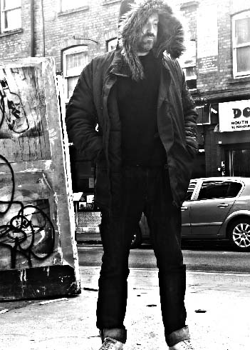 A man in a hooded winter coat stands on a city pavement with his hands in his pockets—a scene captured as contemporary art print. A car and buildings provide an urban backdrop to this original artwork.