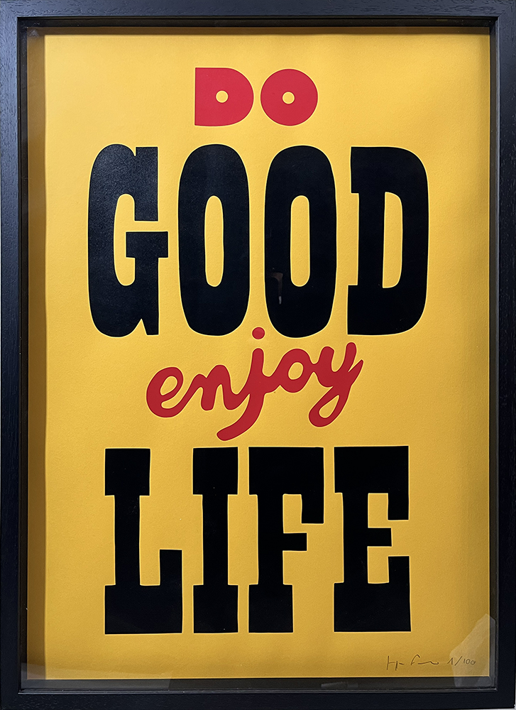 A framed poster with a yellow background and black frame shows the words “DO GOOD enjoy LIFE” in black and red letters.