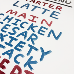 A creatively hand-drawn poster, titled “90’s Menu,” unfolds as a work of art. It colorfully presents a Latte as the introductory starter, followed by main courses such as Chicken Caesar Anxiety Attack, and concludes with indulgent desserts like Chocolate Fudge Pop-Tart Introspection. The entire menu is elegantly scripted in lively shades of red and blue, capturing the essence of the decade with vibrant flair.