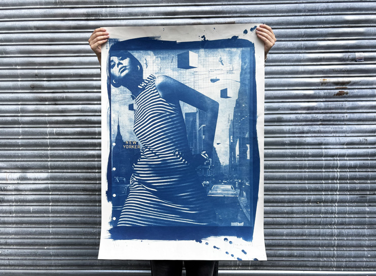 A person holds up a blue-toned Print Club London poster featuring an image of a woman in a striped dress against an urban background, positioned in front of a metal shutter.