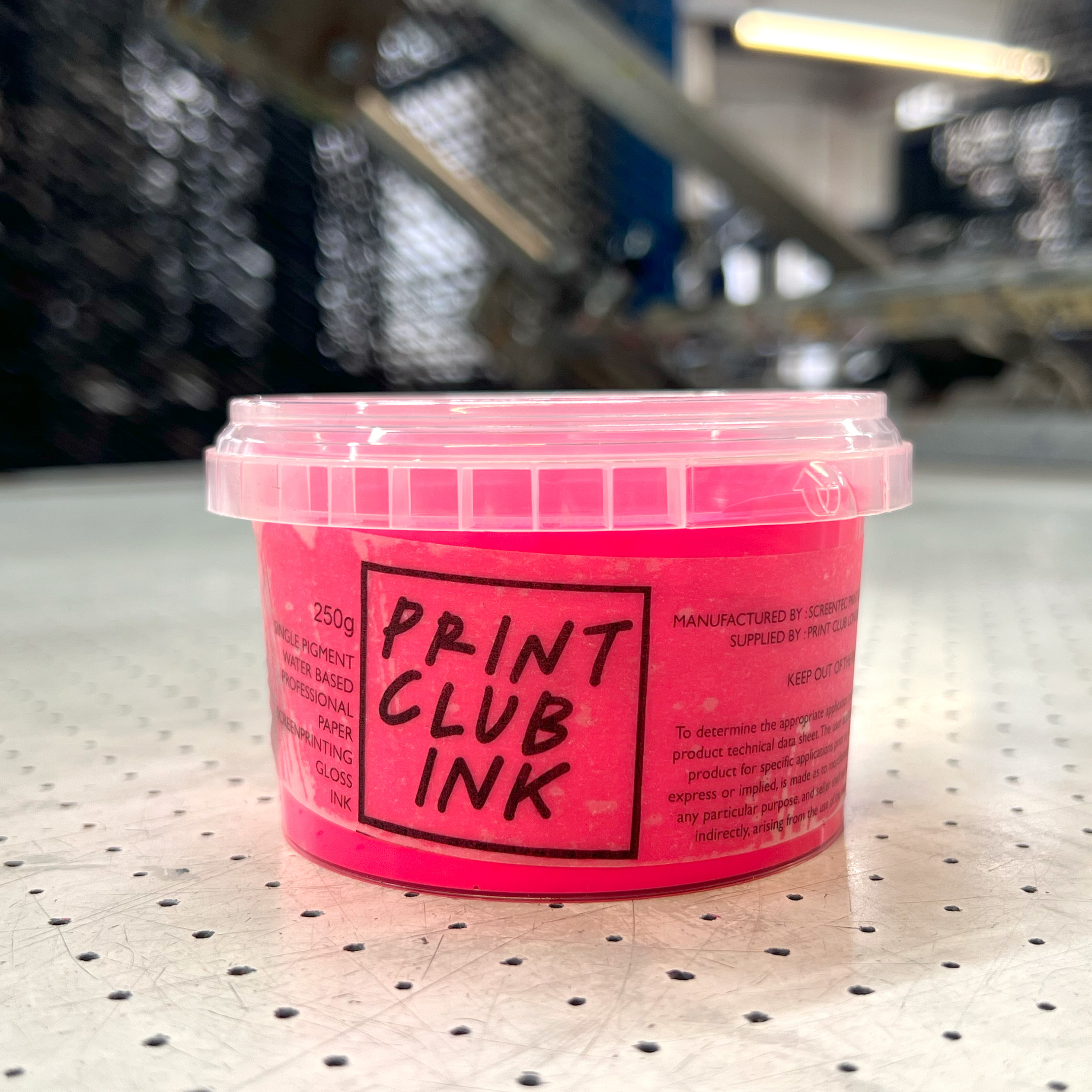 A container labeled "Print Club Inks - Gloss for Paper (Copy)" holds 250g of fluorescent pink pigment-based ink, shown on a perforated metal surface in a workshop.