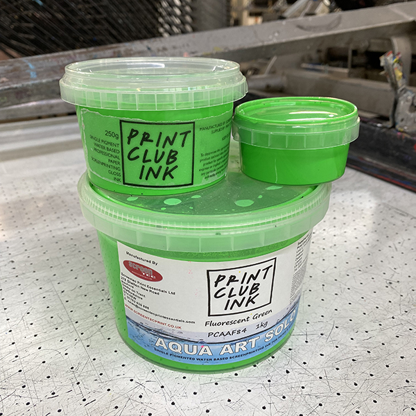 Three containers of fluorescent green "Print Club Ink" sit on a perforated work surface, with one small container placed on top of two stacked larger containers.