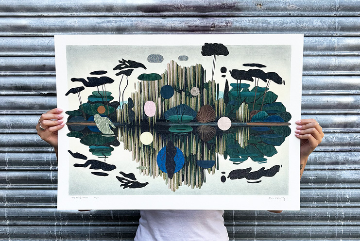 Person holding an abstract artwork from Print Club London, featuring a symmetrical landscape with plants, lily pads, and circular shapes reflected in water, set against a corrugated metal background.