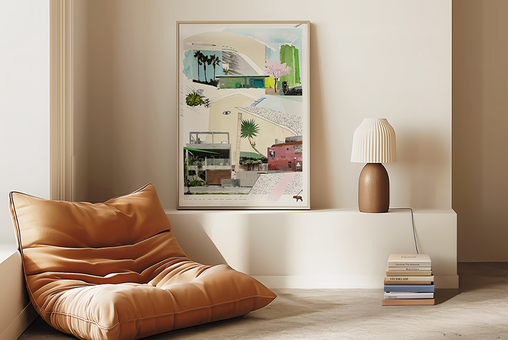 A modern interior features a tan beanbag chair, a Print Club London framed abstract artwork, a table lamp, and stacked books on a low ledge against a cream-colored wall.