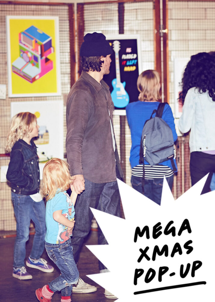 A man holding a child’s hand stands with others inside an art exhibit. Posters are displayed on the wall. Text reads "MEGA XMAS POP-UP.