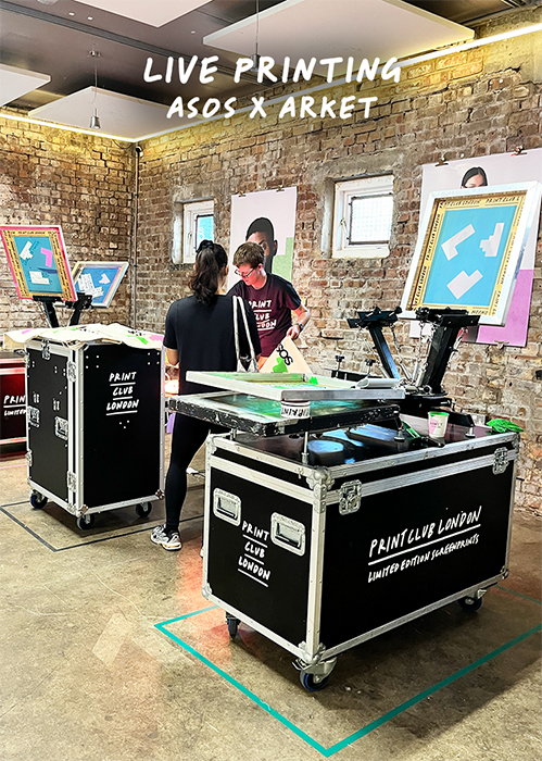 Two people operate live screen printing stations in an industrial-style room with brick walls, featuring ASOS x ARKET event signage and framed prints—a dynamic atmosphere ideal for Live-Events-and-Corporate-Workshops.
