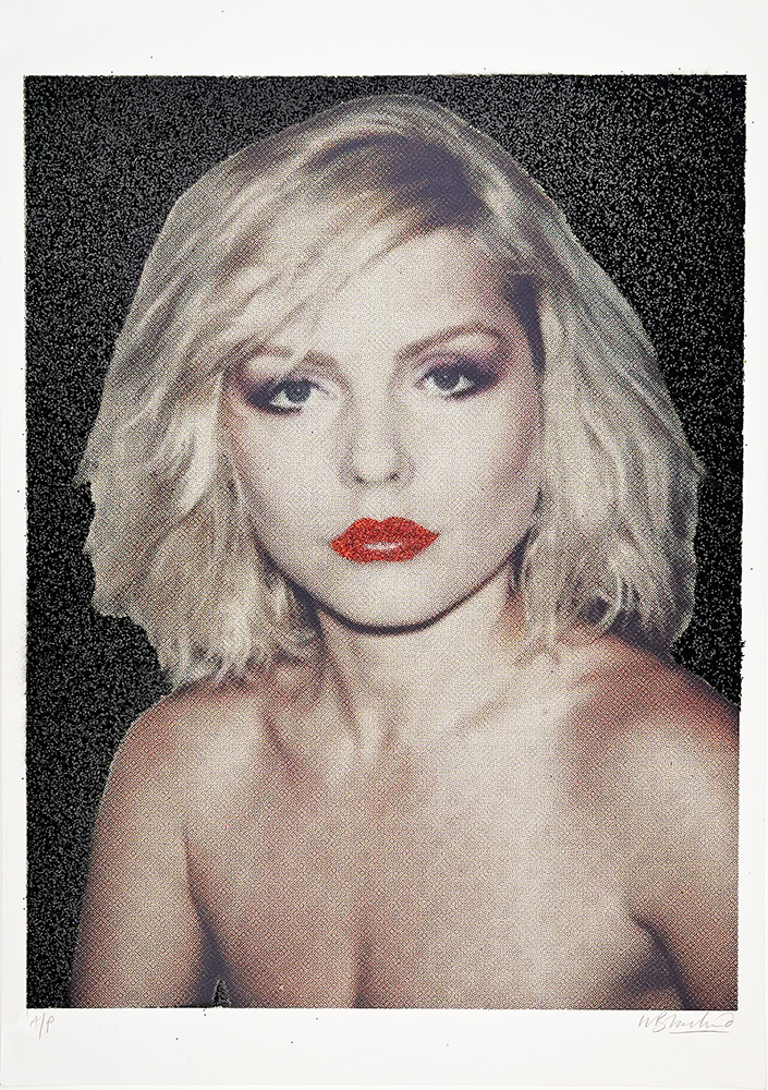 A woman with short blonde hair, red lipstick, and bare shoulders is in front of a black and red glitter-speckled background.