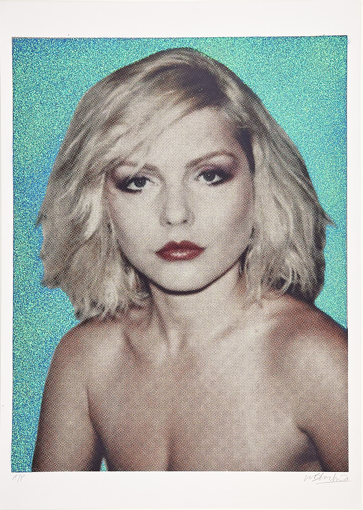 Debbie Harry with short wavy blonde hair and a neutral expression on a textured blue-green background with blue glitter.